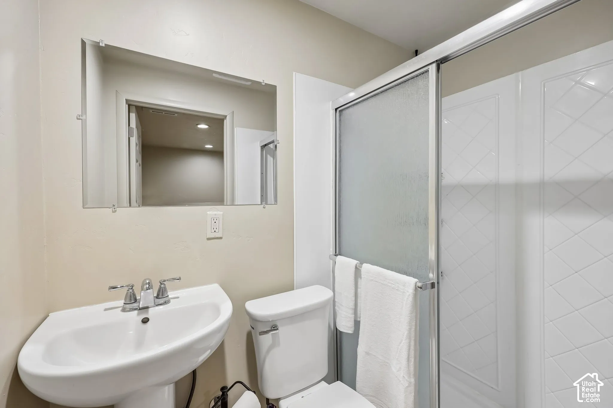 Pedestal sink with chrome faucet, wall-mounted mirror, and glass-enclosed shower with textured wall panels