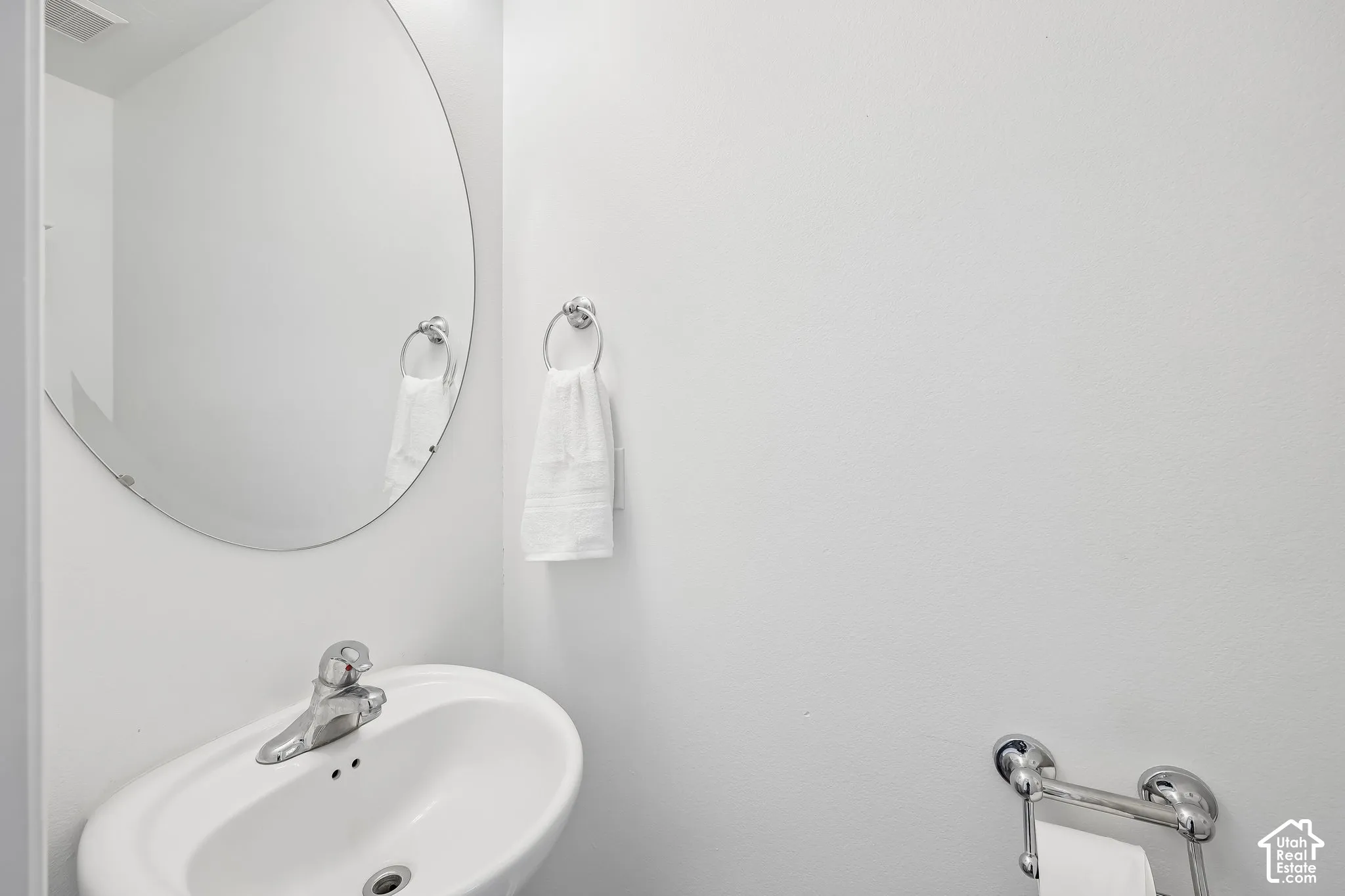 Pedestal sink with chrome faucet, oval frameless mirror, and chrome towel rings