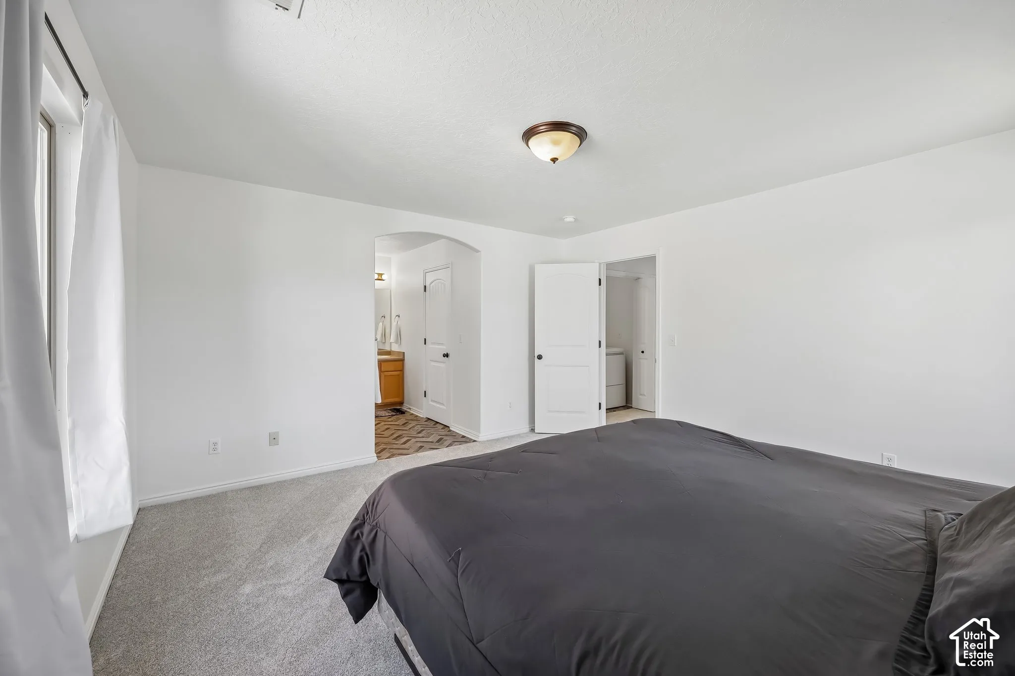 Light-colored carpeting, white walls, and a window with white curtains
