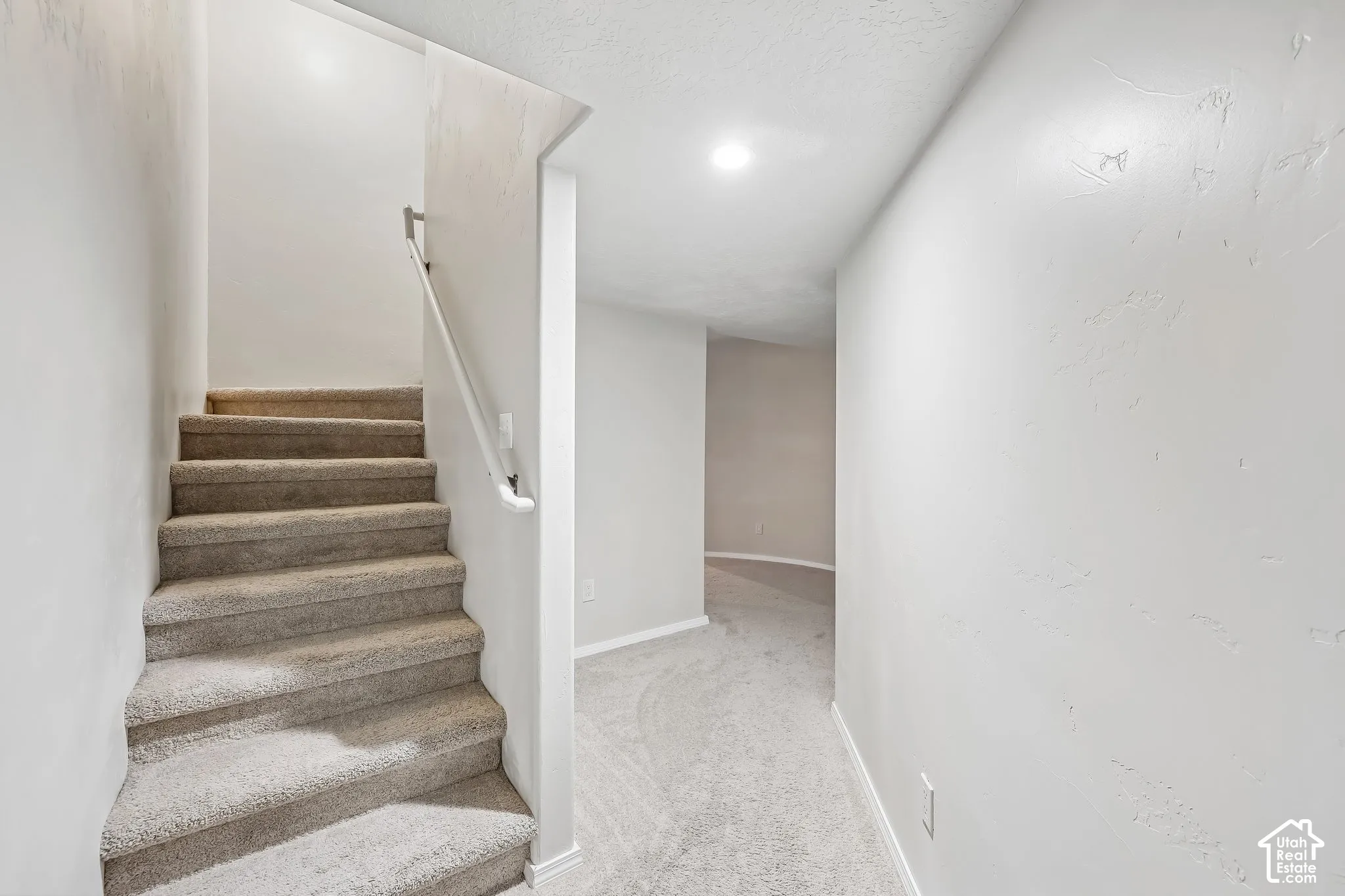 Carpeted staircase with a white handrail, recessed lighting, and light-toned wall finishes