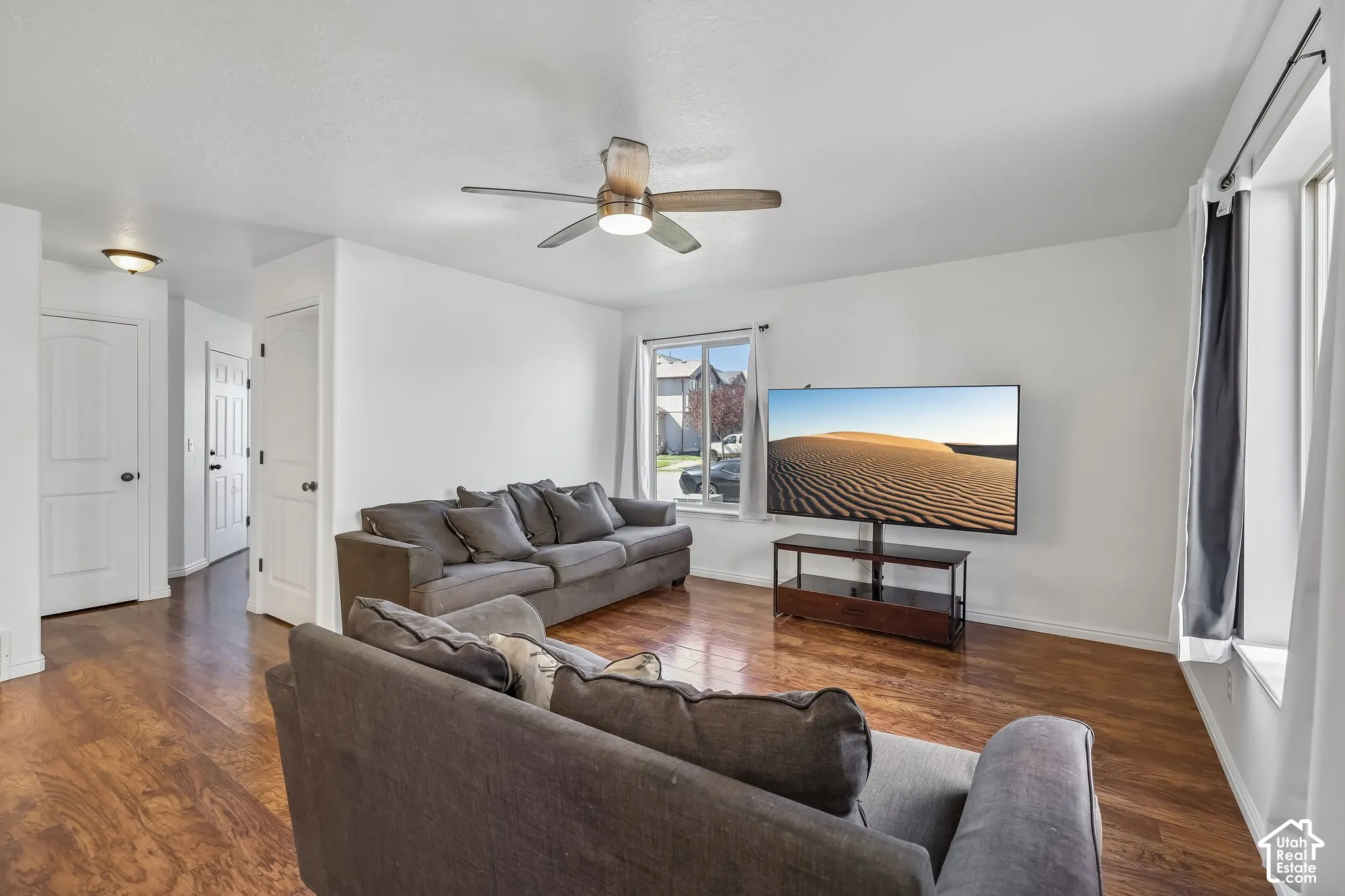 Spacious living area featuring wood-finish flooring, a ceiling fan with integrated lighting, and multiple windows