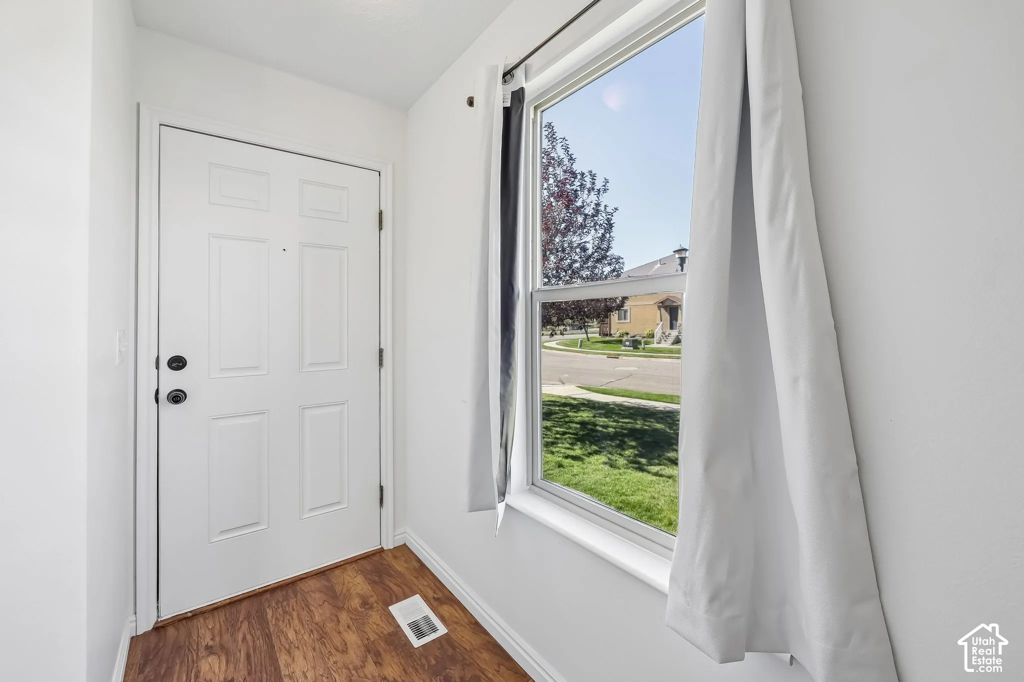 White paneled entry door with black hardware, wood-finish flooring, and a large window