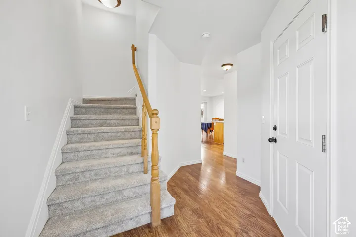 Hardwood-finish flooring, carpeted staircase, light wood-tone handrail, recessed lighting, and panel door