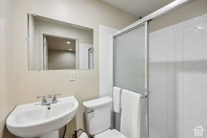 Pedestal sink with chrome faucet, wall-mounted mirror, and glass-enclosed shower with textured wall panels