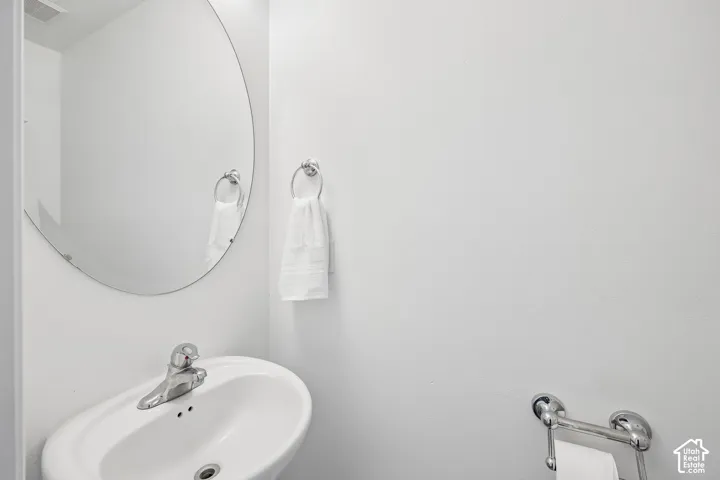 Pedestal sink with chrome faucet, oval frameless mirror, and chrome towel rings