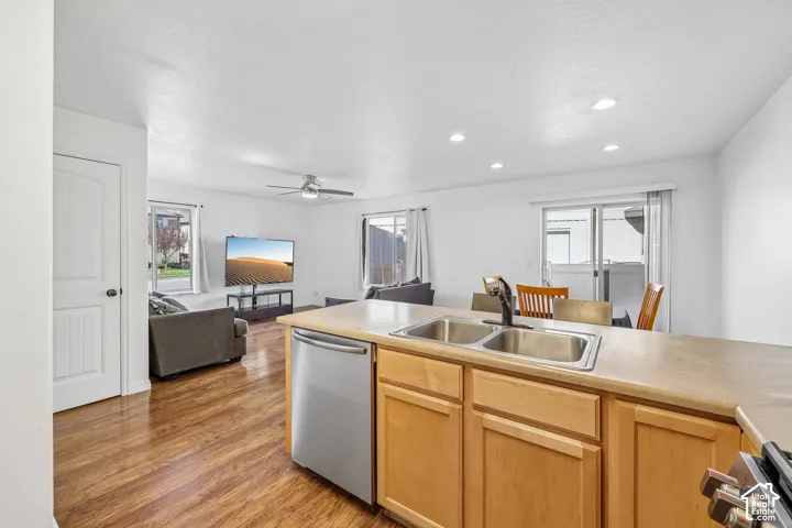 Kitchen island featuring a double basin stainless steel sink, a stainless steel dishwasher, wood-finish cabinetry, and a light-toned countertop