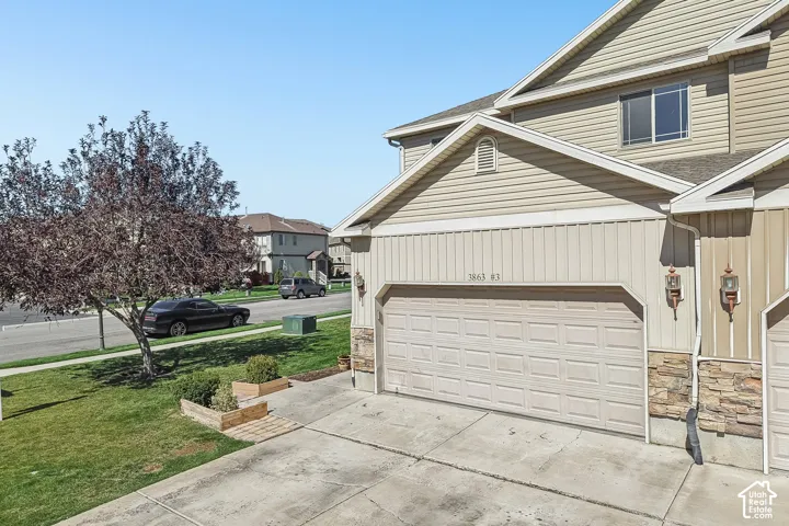 Exterior with siding and stone accents, featuring a two-car garage, concrete driveway, and front lawn with a mature tree
