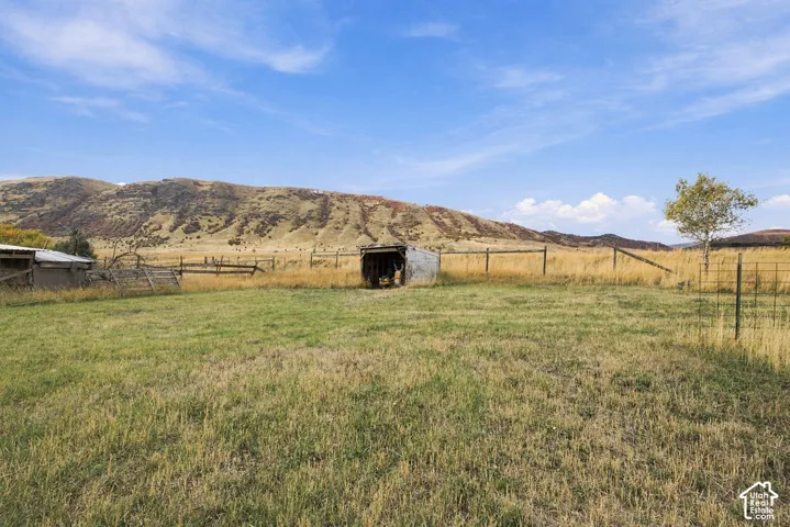 Expansive grassy landscape with distant mountainous terrain, a metal-roofed outbuilding, and varied fencing