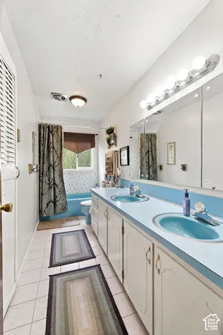 Double vanity with integrated blue sinks, light-colored cabinetry, a large mirrored wall, and overhead strip lighting