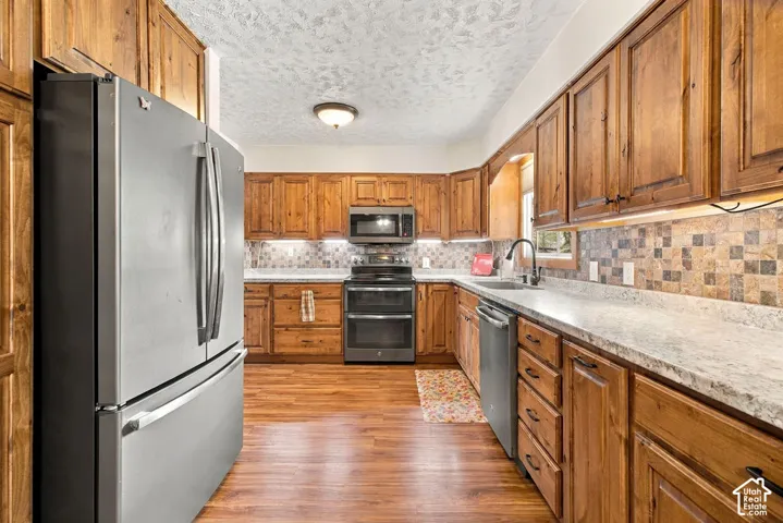 Kitchen featuring wood-finish cabinetry, stainless steel appliances, light-toned countertops, and a patterned tile backsplash