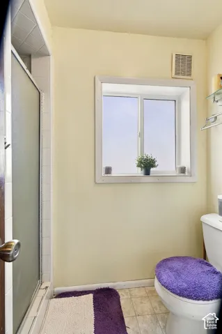 Two-pane window with white trim, shower with frosted glass enclosure, white toilet, and wall-mounted exhaust fan