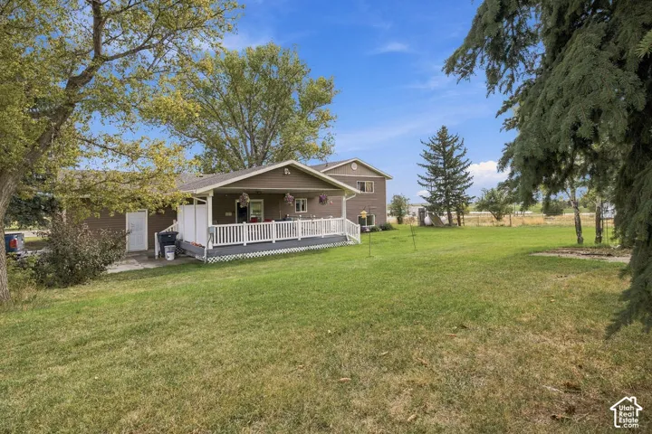 Expansive lawn with mature trees and a residential structure featuring a covered front porch with white railing