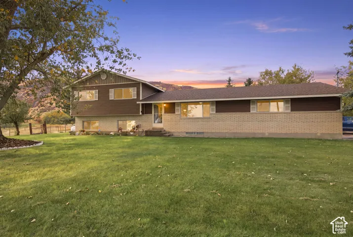 Split-level residence featuring brick and wood siding, a dark shingle roof, and multiple windows with white shutters