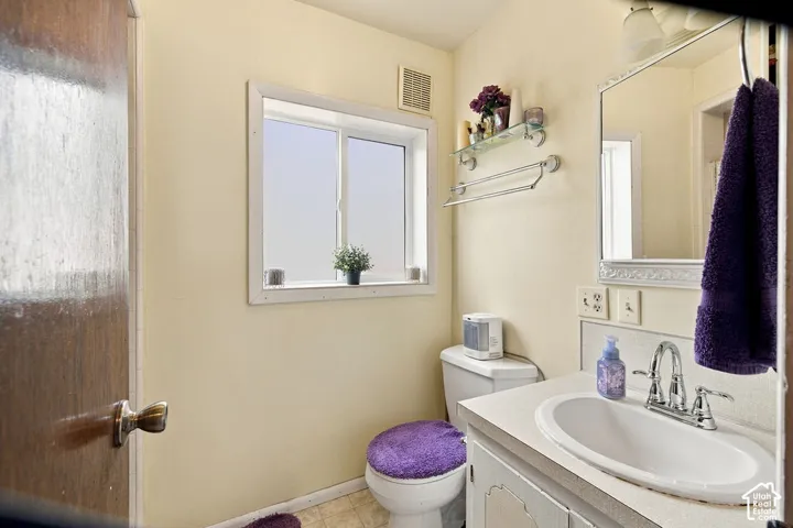 White framed window, wall-mounted exhaust fan, vanity with integrated sink, chrome faucet, and decorative framed mirror
