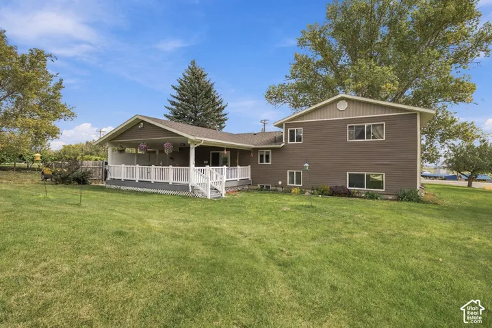 Expansive green space featuring a large rear deck with white railing, covered patio, and multi-level brown siding