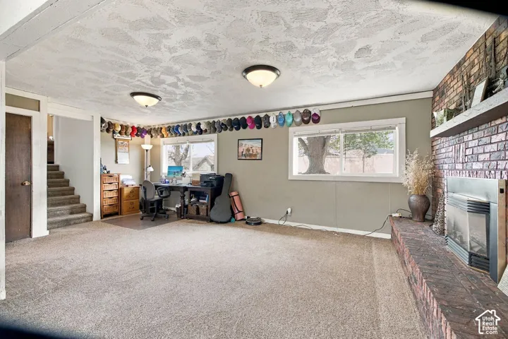 Expansive room with neutral carpeting, two windows, and a brick-finish fireplace with a hearth and mantle