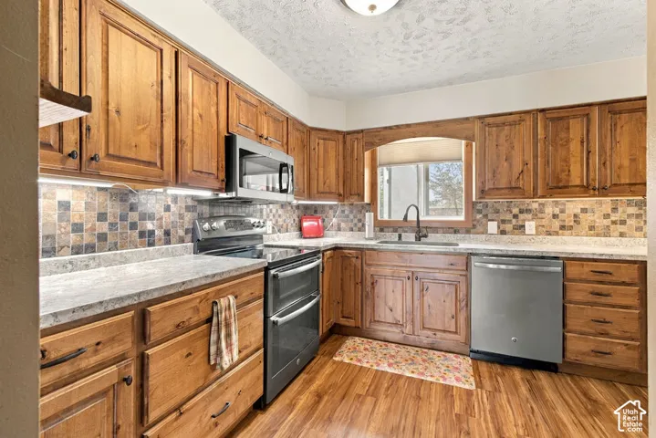 Wood-finish flooring with full-height wood cabinetry, stainless steel appliances, and a tiled backsplash