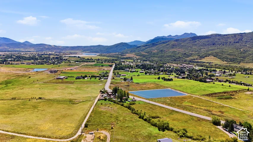Expansive rural landscape featuring a distant body of water, rolling green fields, and surrounding mountains