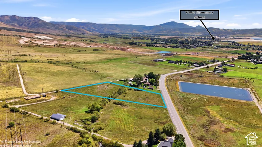 Expansive land parcel featuring open fields, paved road frontage, and mountainous surroundings
