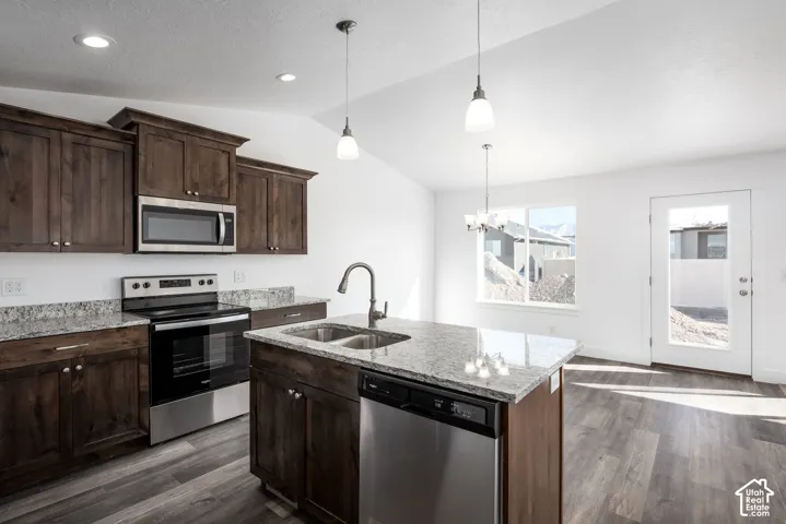 Kitchen featuring wood-finish cabinetry, stainless steel appliances, granite countertops, an island with an integrated sink, and wood-finish flooring