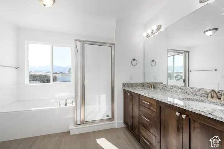 Dual vanity with undermount sinks and granite countertops, separate shower enclosure with clear glass door, built-in bathtub, and large window