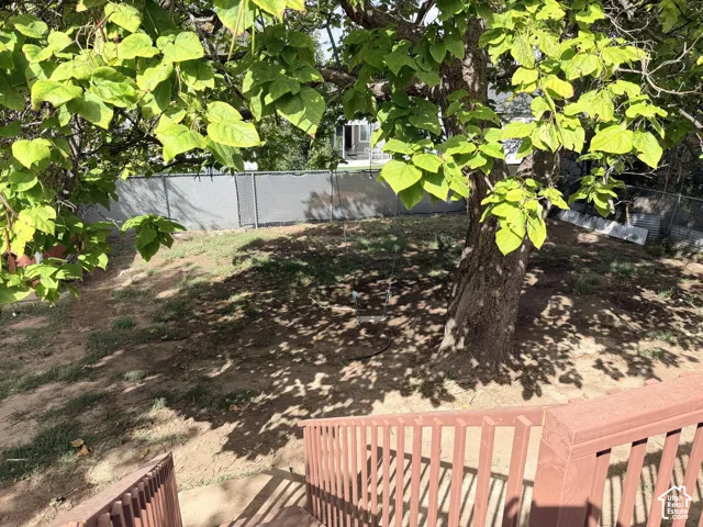 Rear yard with mature tree, sloped terrain, and perimeter fencing