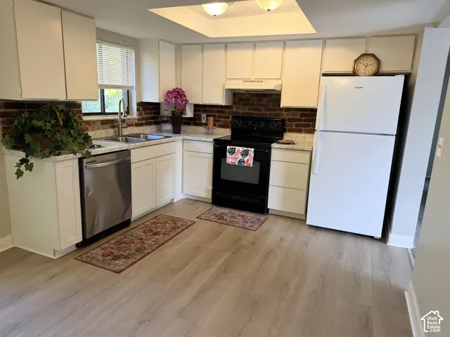 Modern kitchen featuring white cabinetry, a brick-style backsplash, stainless steel dishwasher, and wood-finish flooring