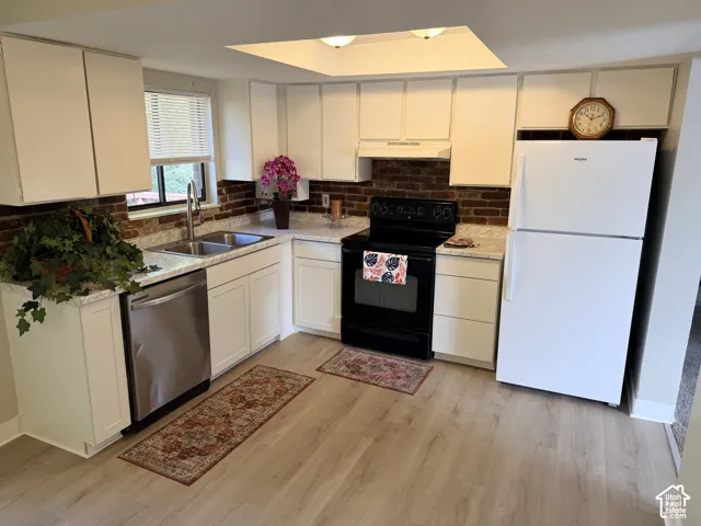 L-shaped kitchen featuring white cabinetry, light-toned wood-finish flooring, a stainless steel dishwasher, a black range, and brick-patterned backsplash