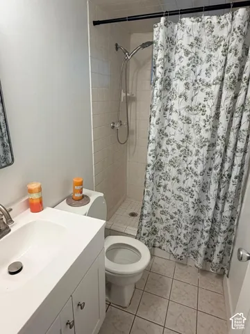 White vanity with integrated sink, chrome faucet, white subway tile shower surround, and tile flooring