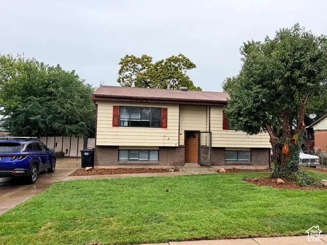 Split-level home featuring a cream and burgundy exterior with updated siding, situated on a manicured lawn with mature landscaping