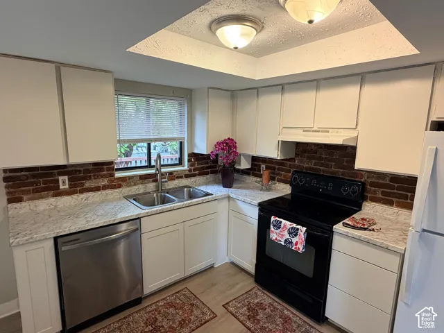 White cabinetry, brick-finish backsplash, light-toned countertops, stainless steel dishwasher, and wood-finish flooring