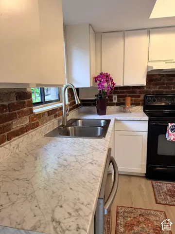 White cabinetry, patterned countertops, stainless steel sink, brick-finish backsplash, and light wood-finish flooring