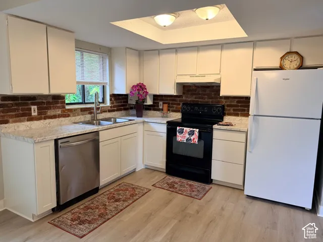 White cabinetry, light-toned wood-finish flooring, brick-patterned backsplash, stainless steel sink, and a stainless steel dishwasher