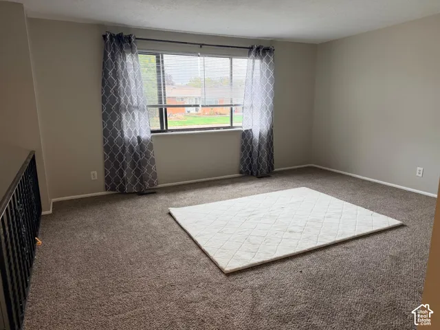 Carpeted flooring, neutral wall tones, large window with blinds, and white trim
