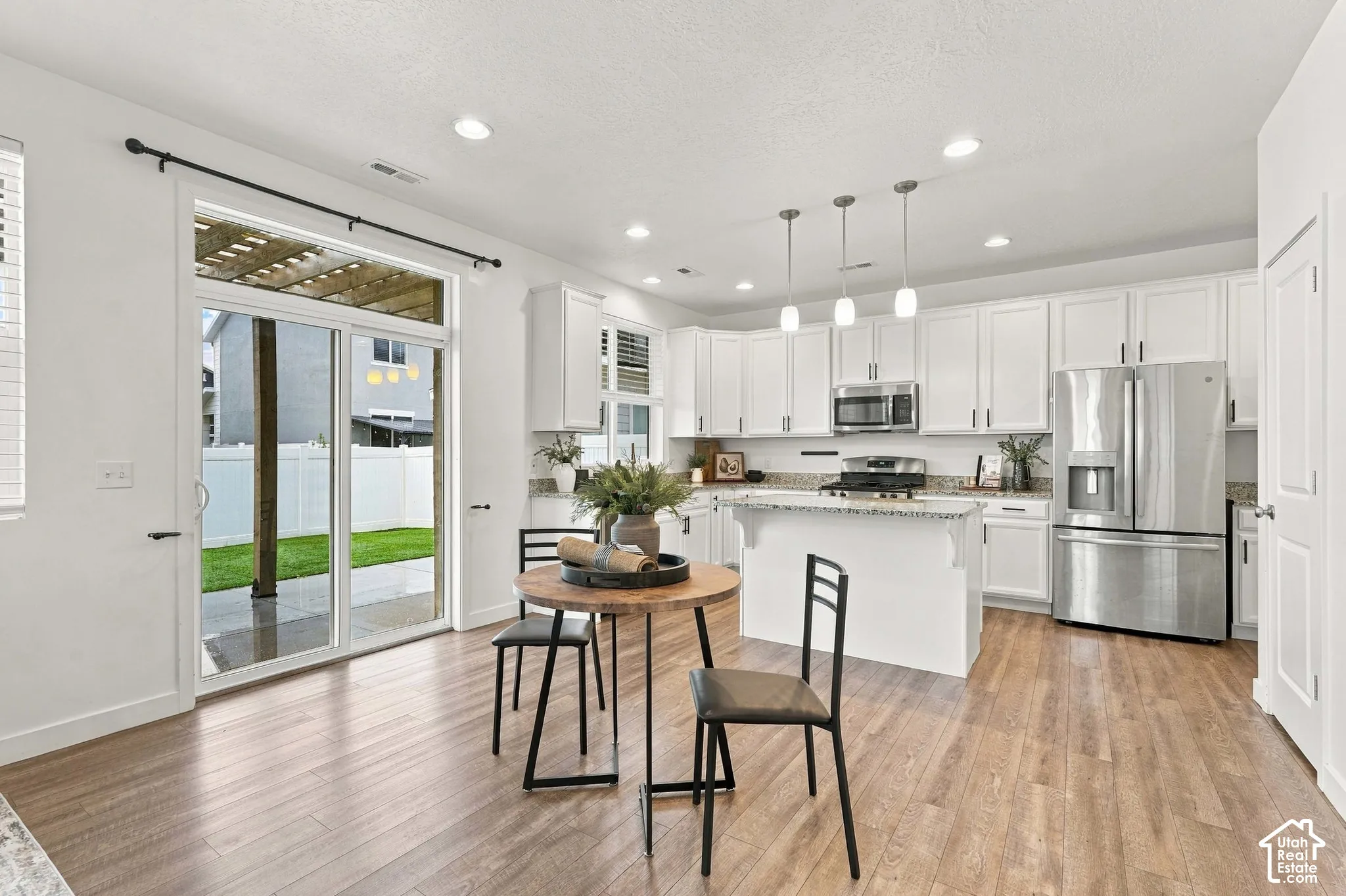 White shaker cabinetry, stainless steel appliances, wood-finish flooring, recessed lighting, and sliding glass door access to a patio