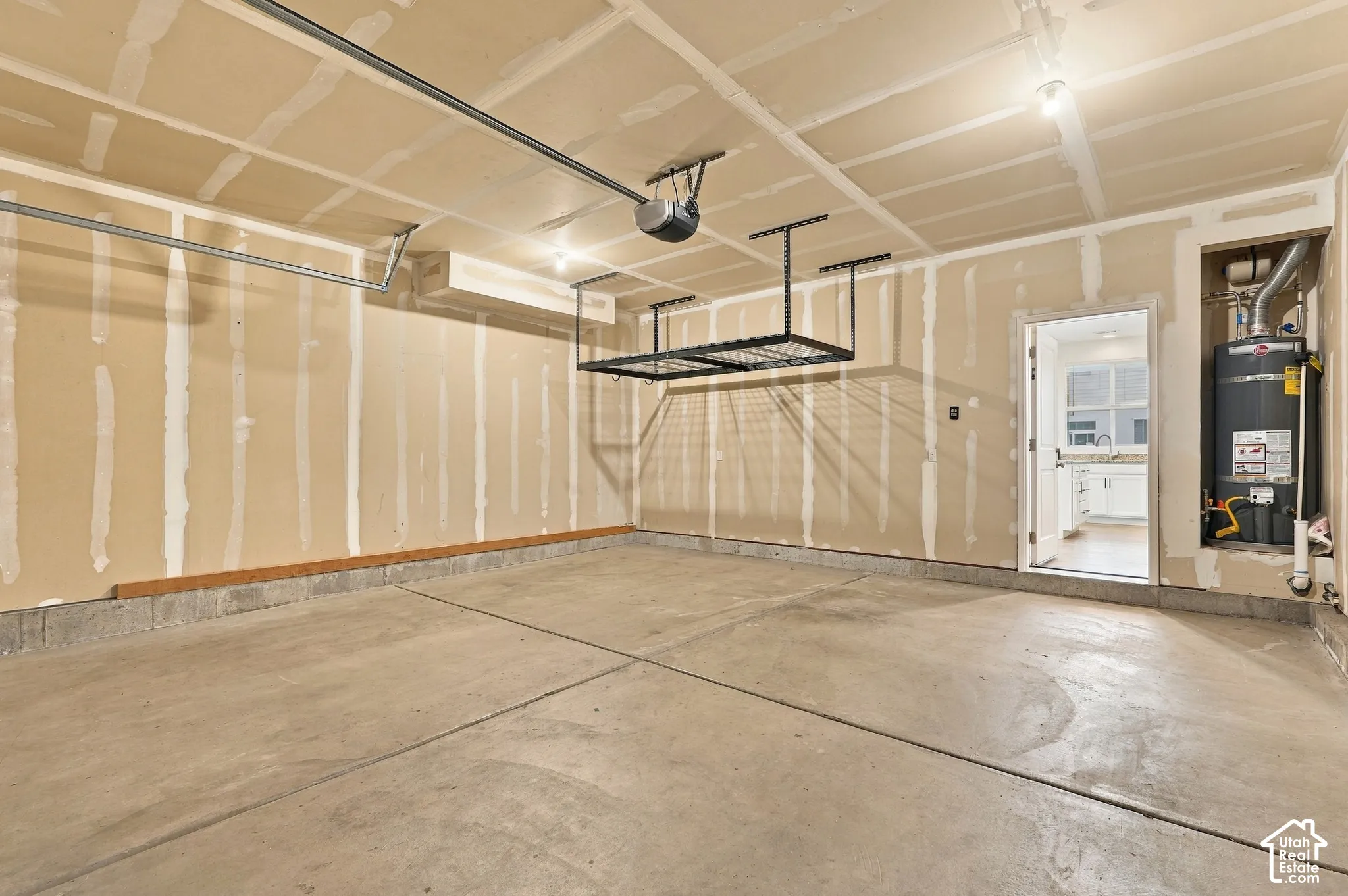 Concrete flooring, overhead storage racks, garage door opener mechanism, exposed ceiling joists, and a utility niche