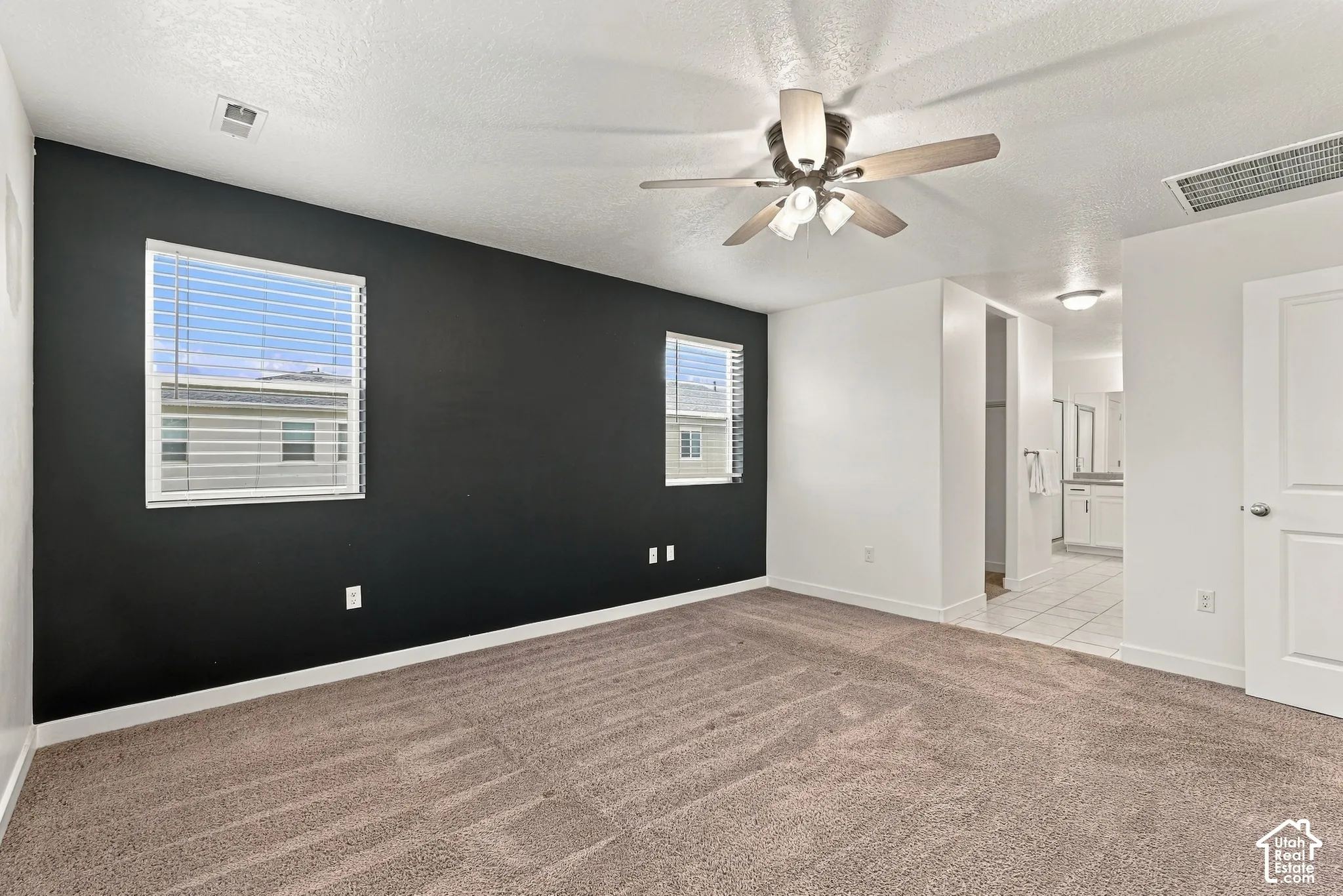 Carpeted room with a dark accent wall, two windows with blinds, and a ceiling fan with integrated lighting