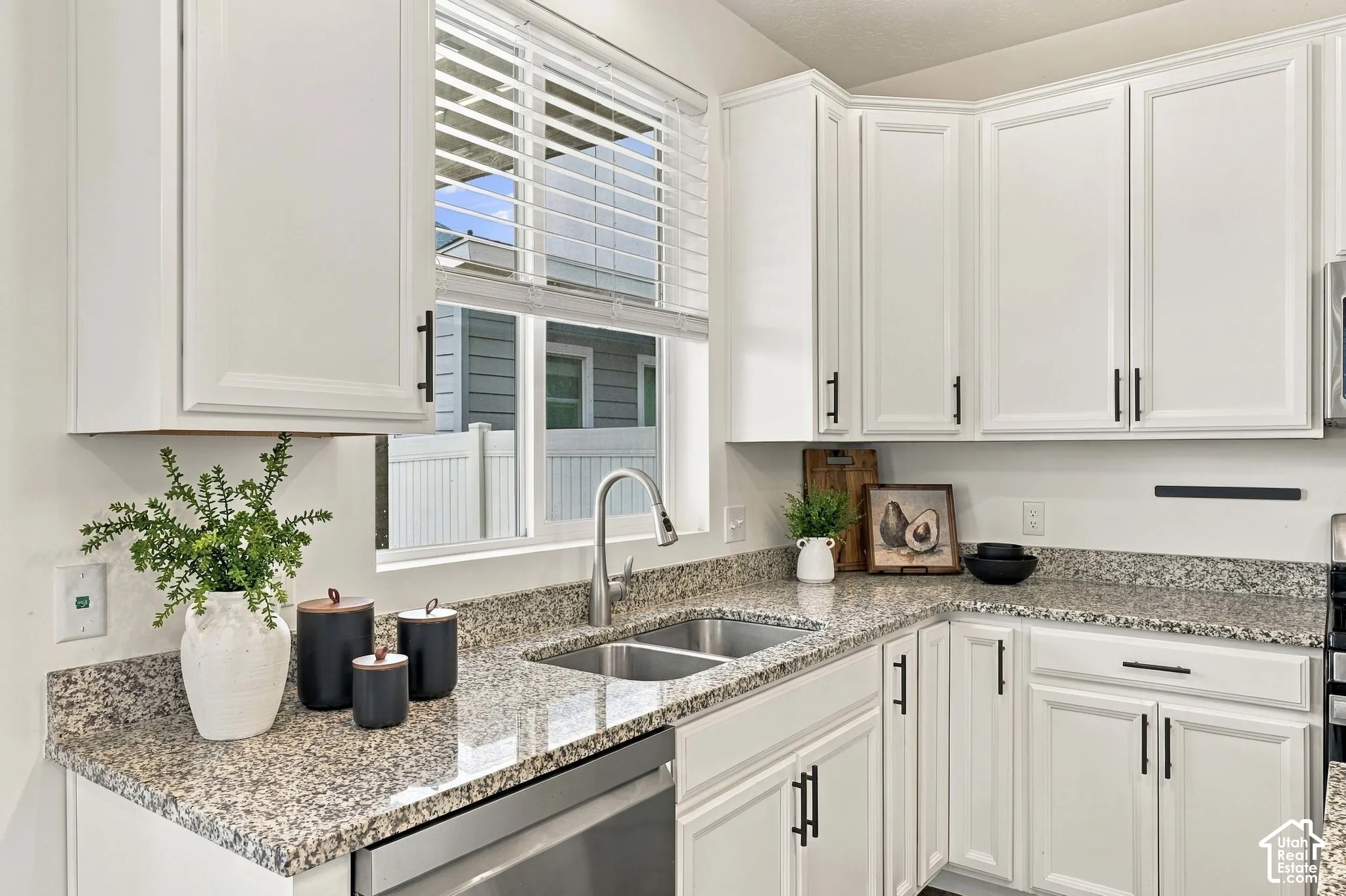 White shaker-style cabinetry with matte black hardware, granite countertops, stainless steel undermount double-basin sink, and a stainless steel dishwasher
