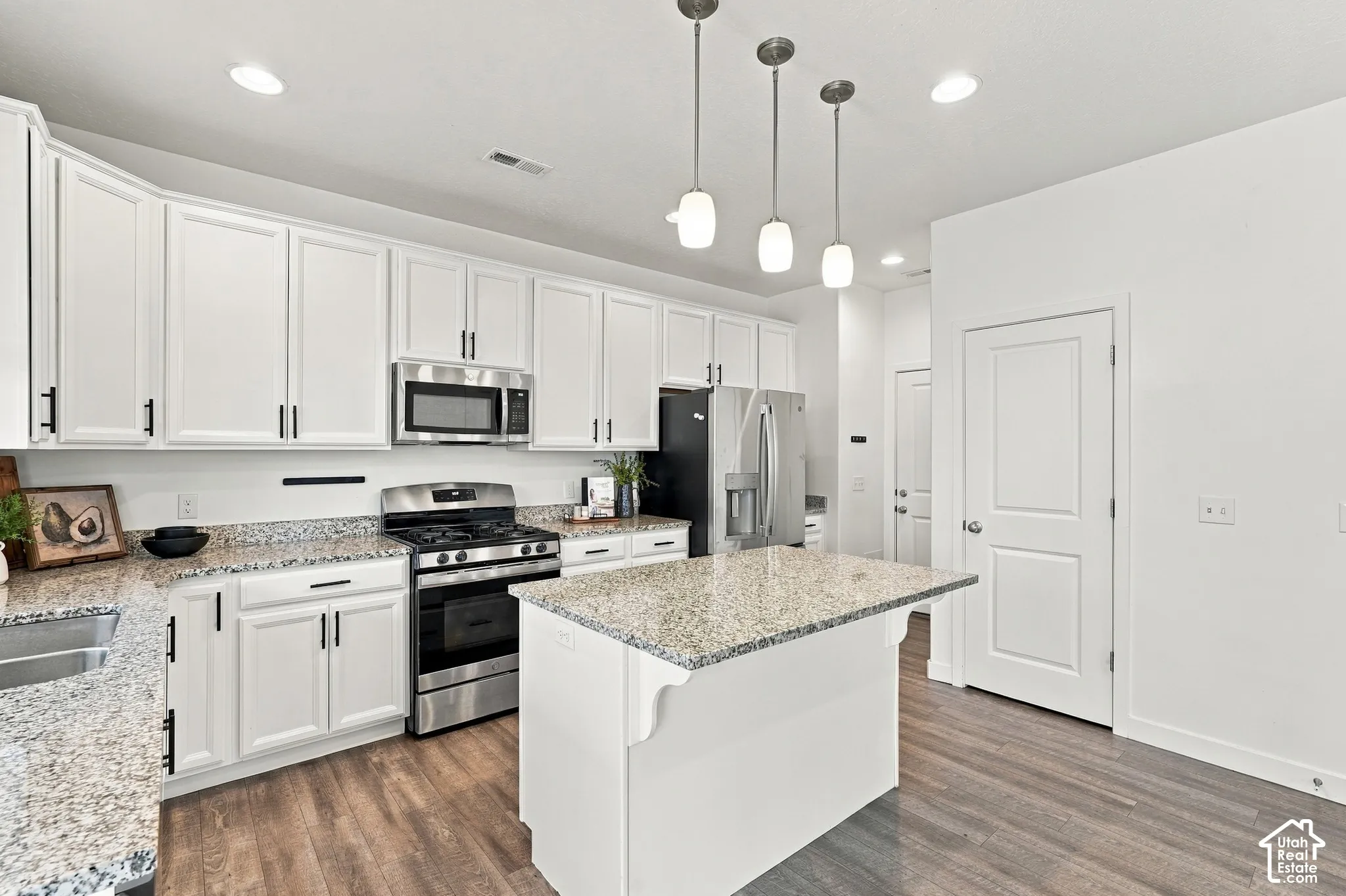 White cabinetry with matte black hardware, stainless steel appliances, granite countertops, wood-finish flooring, and a central island