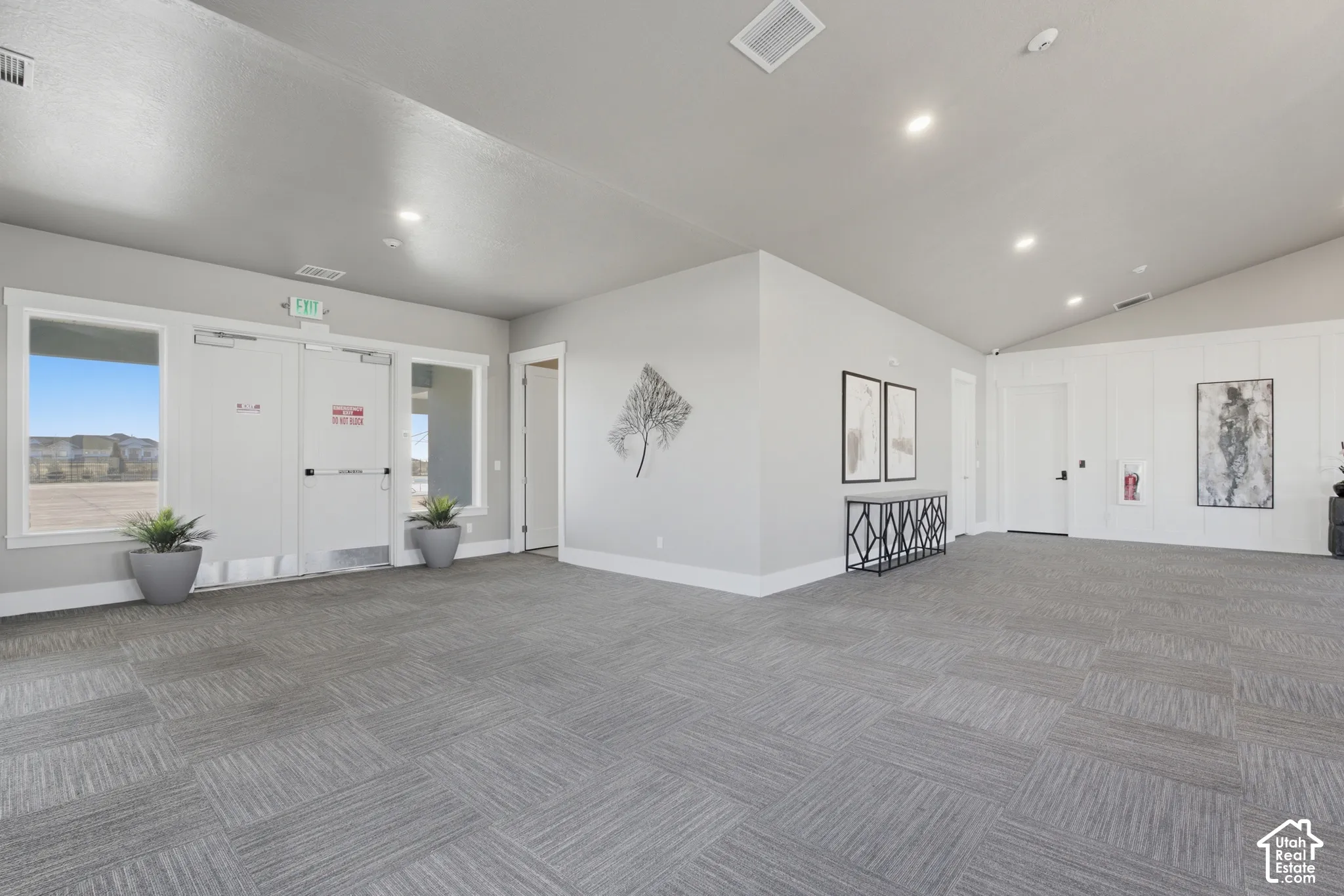Recessed lighting, sloped ceiling, gray carpet tile flooring, white paneling, and multiple windows