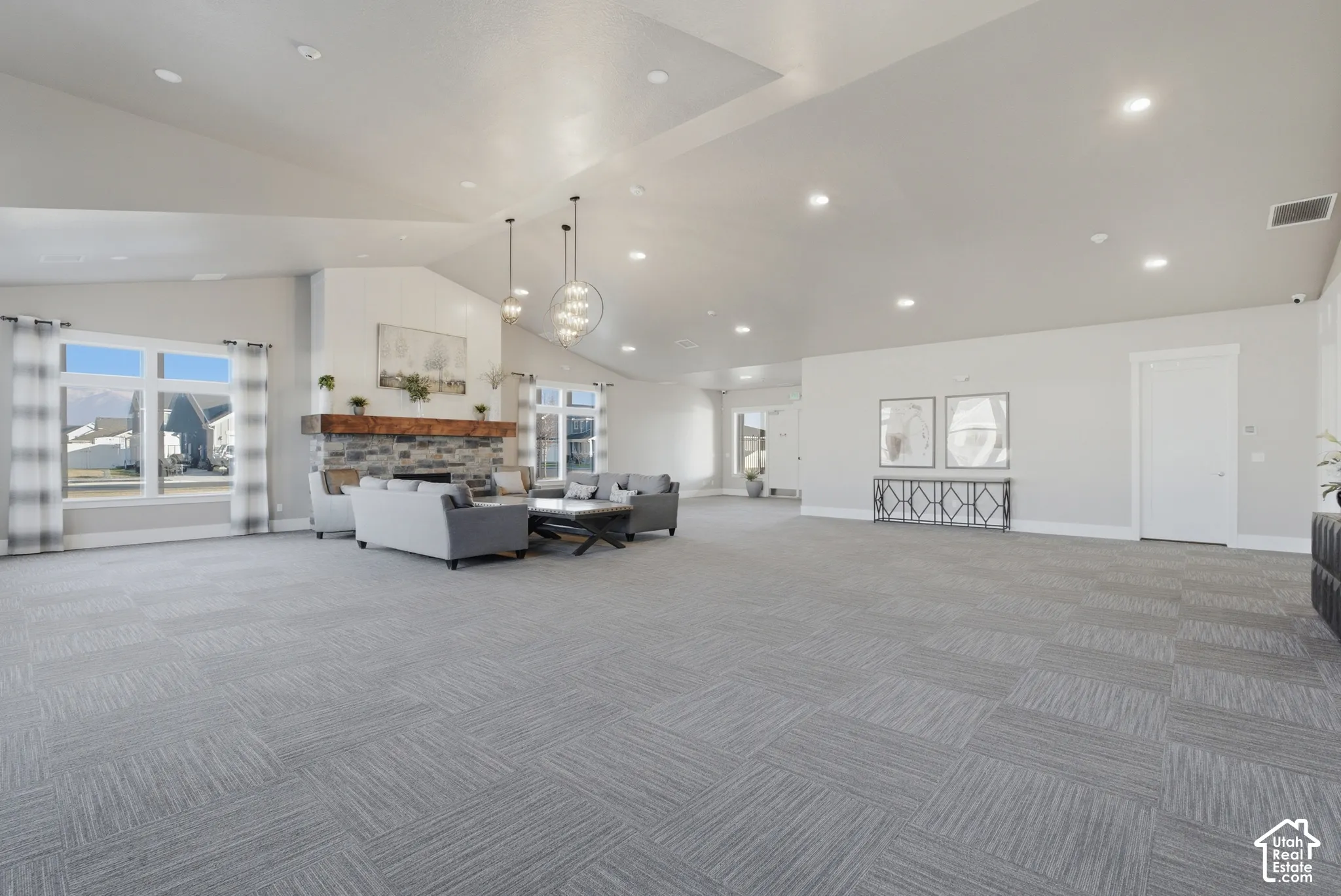 Vaulted ceilings, recessed lighting, stone fireplace with wood mantel, large windows, and patterned carpet