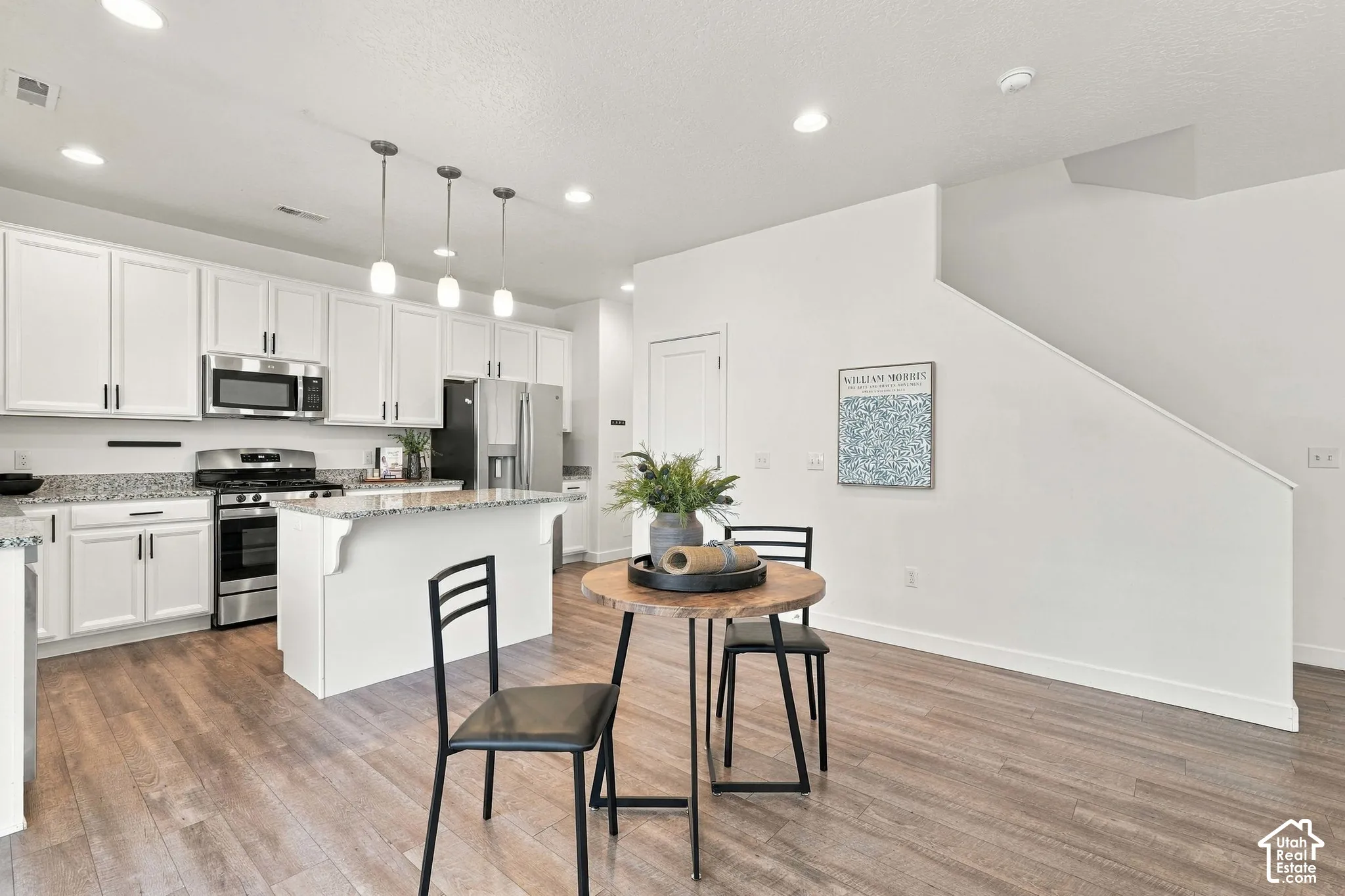 Kitchen featuring white cabinetry, stainless steel appliances, granite countertops, an island with seating, and wood-finish flooring