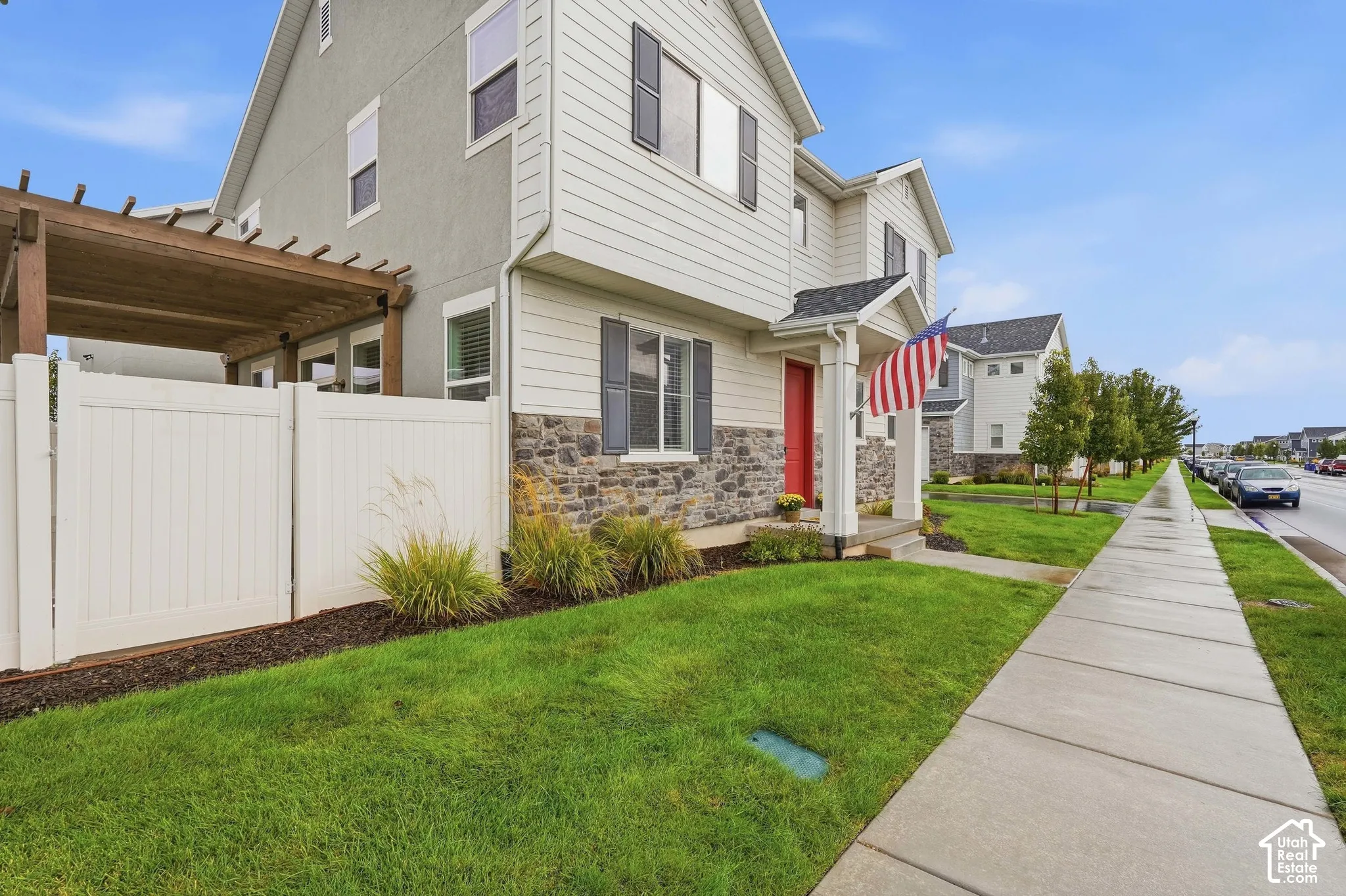 Exterior featuring stone facade, light siding, a vibrant red entry door, an attached pergola, and a white privacy fence
