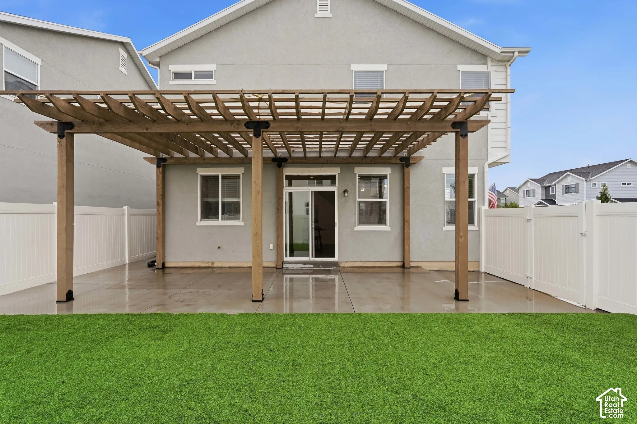 Expansive concrete patio with a wooden pergola, sliding glass door access, and a manicured lawn
