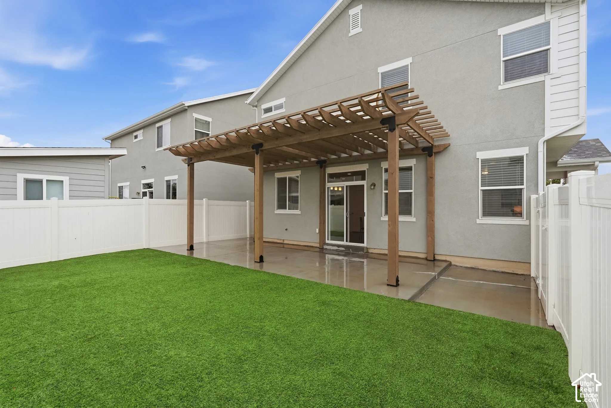 Pergola-covered concrete patio leading to a synthetic turf backyard