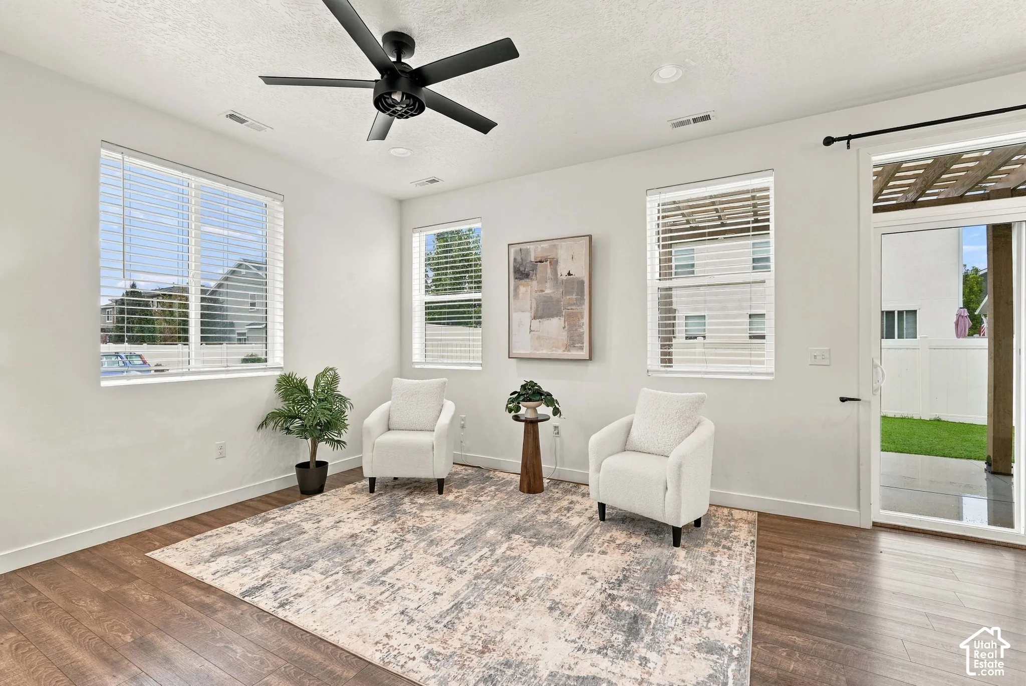 Wood-finish flooring, multiple windows with blinds, ceiling fan, recessed lighting, and a sliding glass door with an overhead trellis