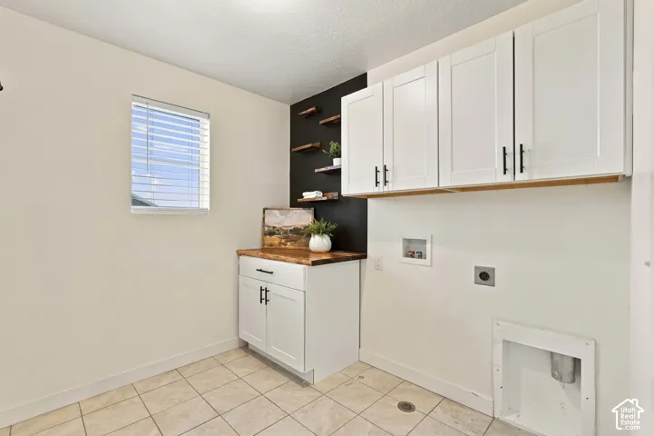 Laundry room featuring tile flooring, white shaker cabinetry with black hardware, wood-finish countertops, and open wood-finish shelving