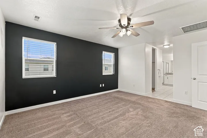 Carpeted room with a dark accent wall, two windows with blinds, and a ceiling fan with integrated lighting