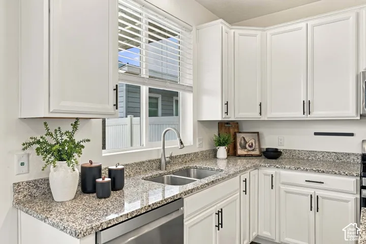 White shaker-style cabinetry with matte black hardware, granite countertops, stainless steel undermount double-basin sink, and a stainless steel dishwasher