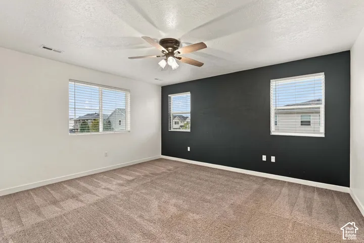 Carpeted flooring, three windows with blinds, ceiling fan with light fixture, and a contrasting accent wall